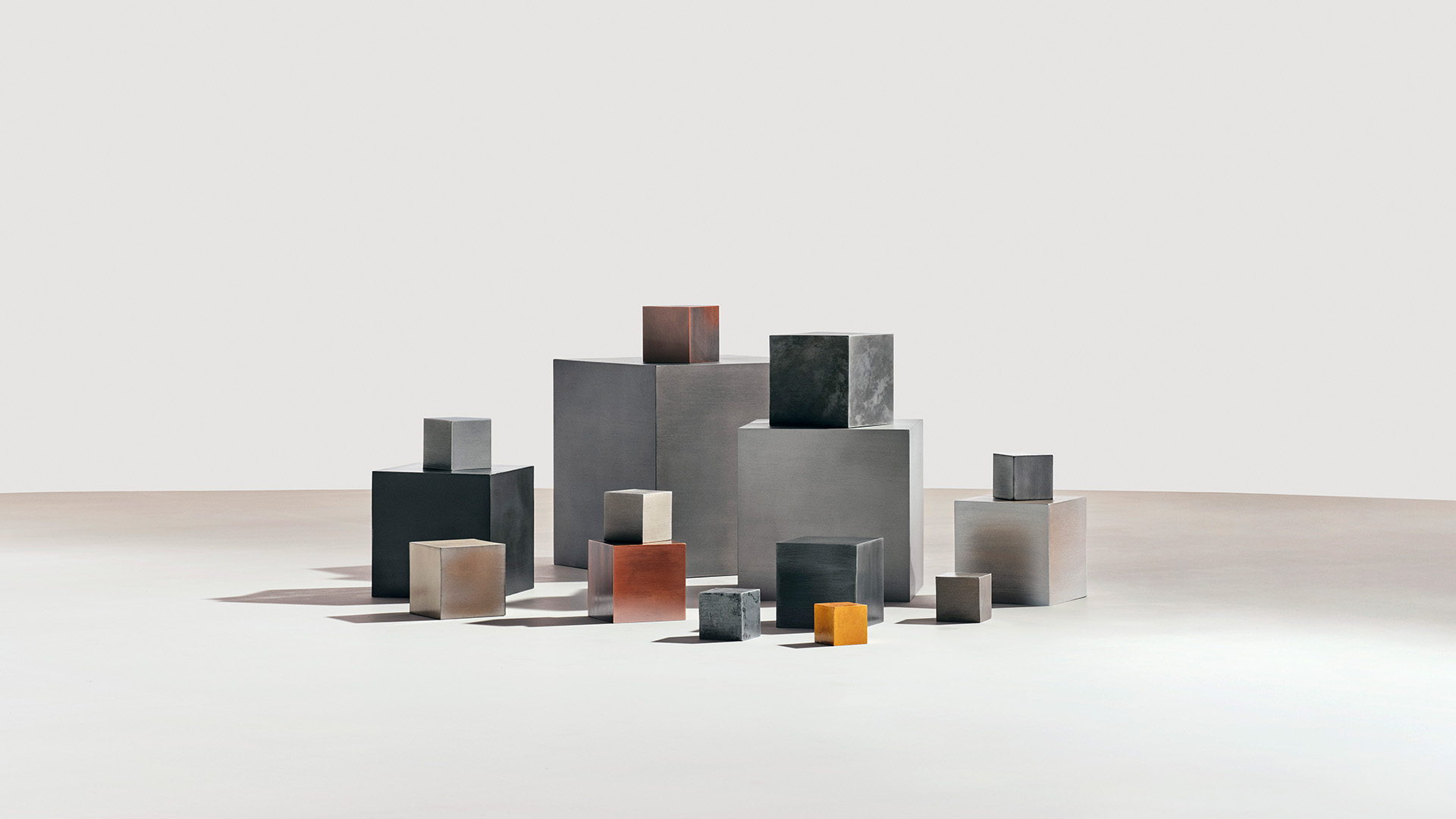 Various metal cubes of different sizes and finishes arranged on a white surface with shadows.