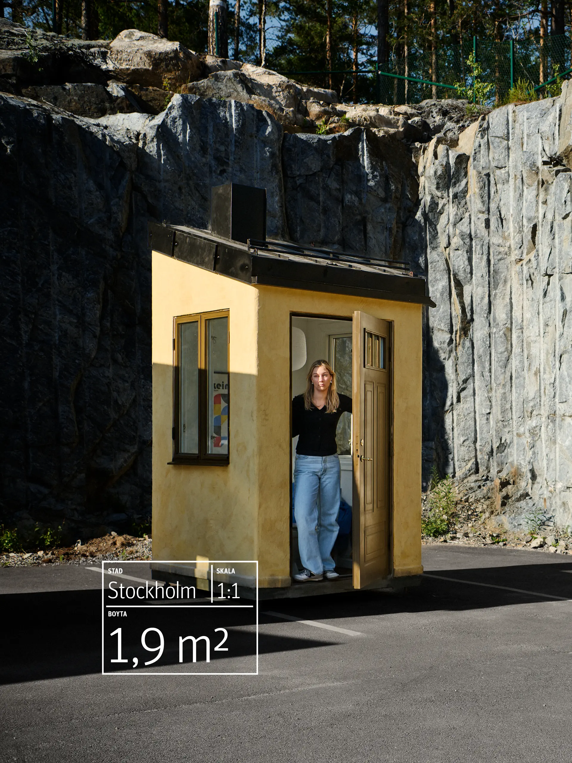 A woman stands in the doorway of a tiny yellow house against rocky cliffs and pavement. The text reads "Stockholm, Scale 1:1, 1,9m2"